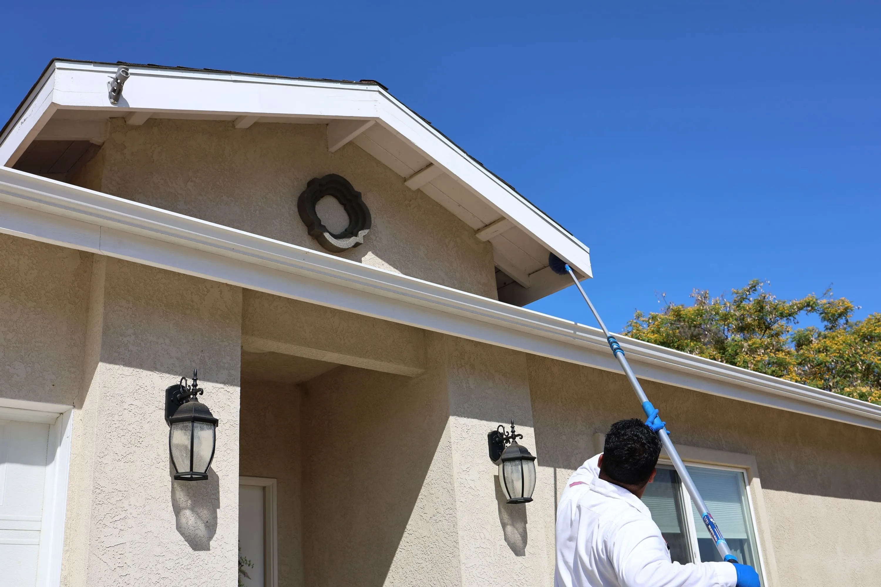 Hydrex Pest Control San Diego technician removing spider webs from a home’s eaves